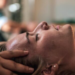 Homme allongé, yeux fermés, recevant un massage avec les mains sur la joue et le cou, dans un décor de spa.