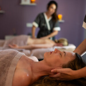 Masseuse allongée sur une table de massage, mains sur le torse d’une cliente, en institut de bien-être avec éclairage doux et arrière-plan flou