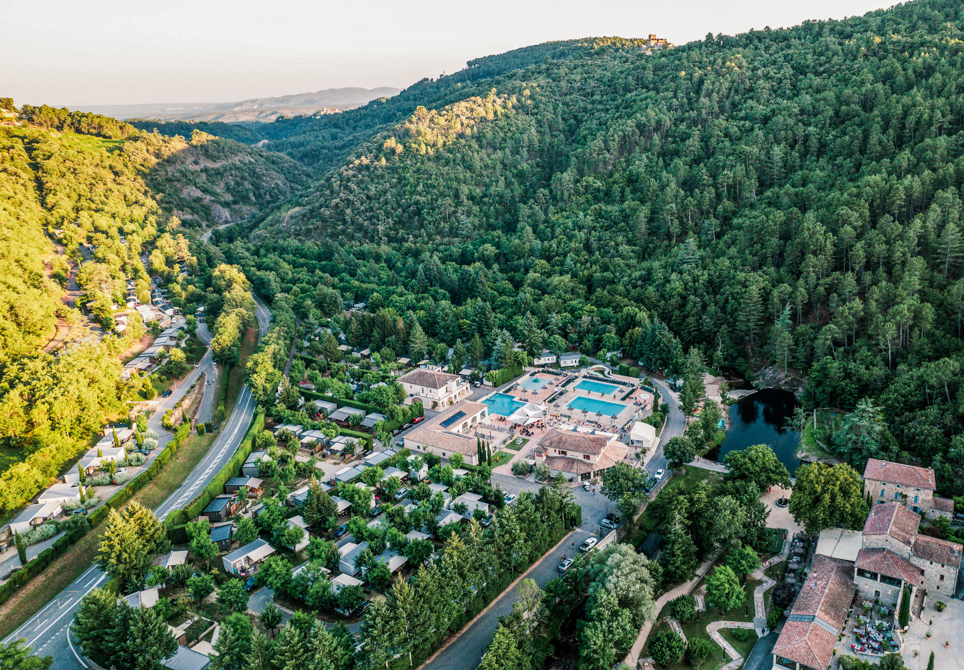 Vue aérienne du camping les Ranchisses niché dans une vallée boisée avec piscines et hébergements